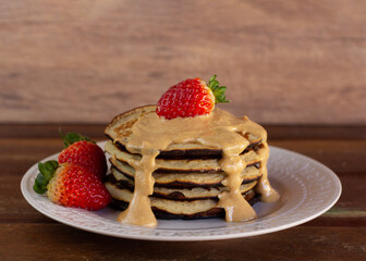 Pile of pancakes with strawberry and sauce of peanut butter, on white plate