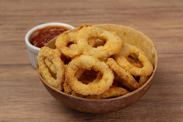 Onion rings in brown bowl on wooden table ans red sauce or ketchup aside