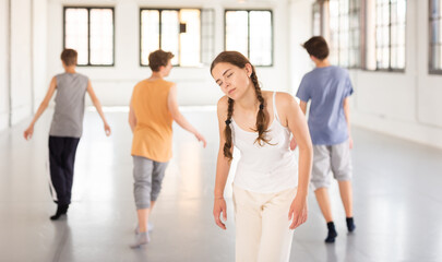 Focused teenage girl performing contemporary dance elements during group dance training in studio