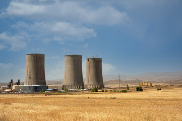 Nuclear power plant cooling towers, big chimneys beside Wheat field with partly cloudy sky in...