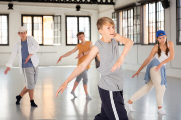 Fototapeta na wymiar Smiling teenage boy having group dance training in studio, performing dynamic elements