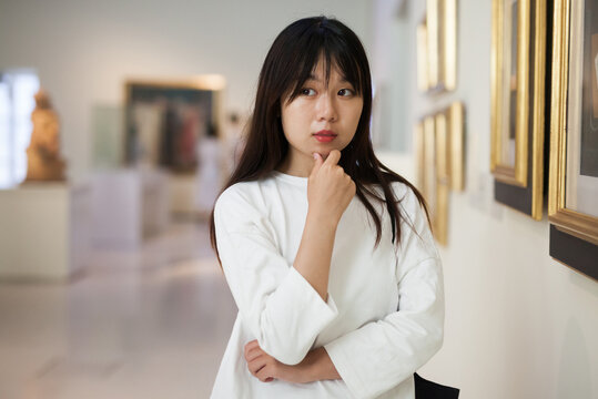 Thoughtful chinese woman standing in art museum near the painting in baguette