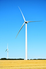 A image of tall wind turbines in an agricultural field a harvest time. 