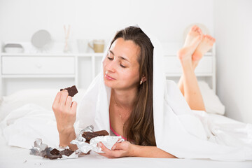 Adult woman secretly eating chocolate under sheets in bed. High quality photo