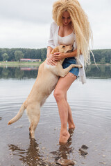 Young woman playing with her labrador retriever dog in river.