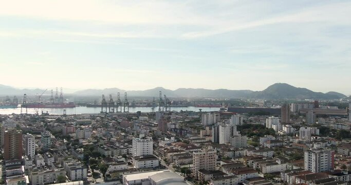 Aerial view of Santos Port River and busy industrial city. slow drone shoot from cranes in Santos Port in Brazil. buildings and houses. 