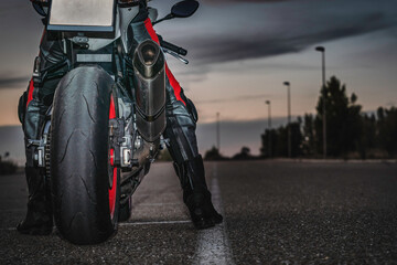 biker sitting on black sports motorcycle on asphalt road dusk under cloudy sky. copy space.