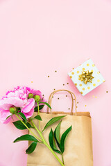 Flat lay of a gift box, a shopping bag and a peony flower over pink background. Copy space.