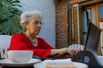 Older adult woman, working or studying on laptop while having breakfast at home.