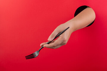 A female hand holds black cutlery on a red background.