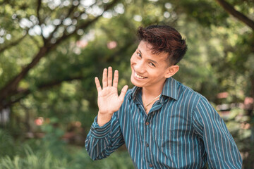 A comical and funny Filipino guy saying hi. Possibly mocking or just having fun. Outdoor scene.