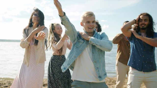Portrait of cheerful girls and guys friends dancing and fooling around outside on beach enjoying summertime. Freedom and positive emotions concept.