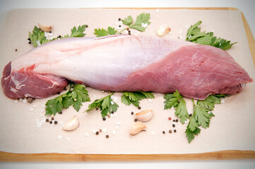 Beef tenderloin. A large piece of meat with vegetables and fresh herbs on a wooden cutting board.