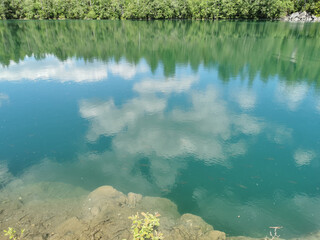 The shore of the lake is bright with clear water, in which you can see the marble on the bottom and reflect the sky with clouds, in the mountain park Ruskeala.