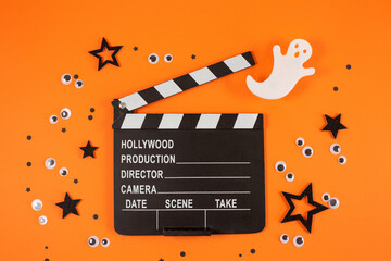 Clapper board in spider webs, spiders, ghost, eyes on orange background.