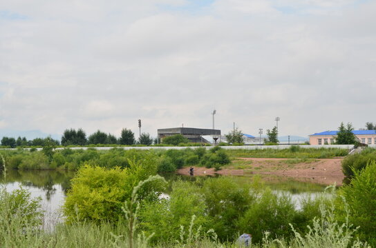 A river with bushes, fisherman and stadium