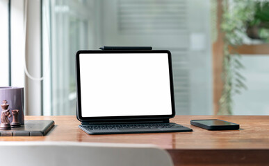 Blank screen tablet with magic keyboard and smartphone on wooden table in living room.