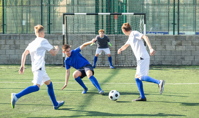 Game moments of football match between two teams of teenagers in white and blue shirts