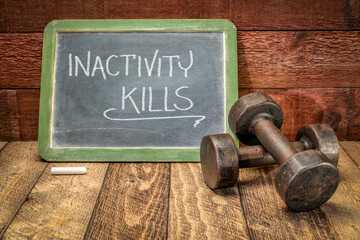 inactivity kills motivational concept, white chalk writing on a slate blackboard with a pair of vintage dumbbells, sedentary lifestyle, fitness and personal development