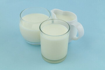 Jug with milk and two glasses of milk on blue background.
