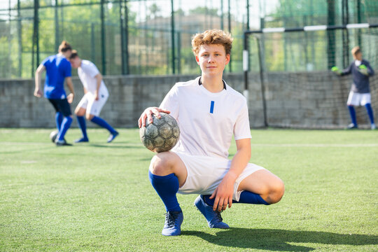 Junior football player sitting on on field with ball
