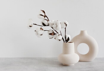 Modern beige ceramic vases with dry  cotton branches on gray table near a white wall. Copy...