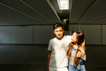 Portrait of happy young Vietnamese couple in love hugging when standing in sunrays on underground parking