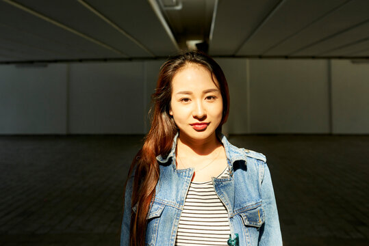 Portrait Of Pretty Young Asian Woman In Striped Shirt And Denim Jacket Looking At Camera