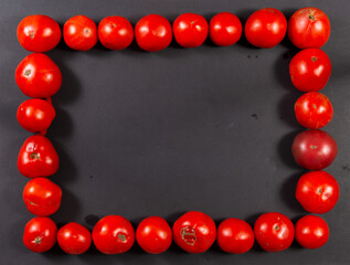 Rectangular frame of red tomatoes on a black background. Horizontal.