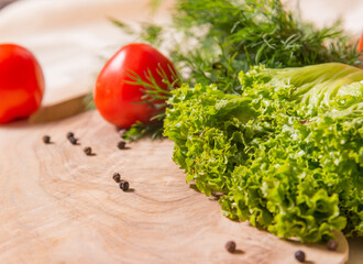 Fragment of cutting board made of olive tree, on which lie lettuce, dill, tomatoes.