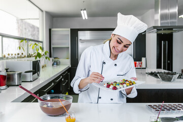 young hispanic woman chocolatier in chef hat with mexican chocolates candies on plate in a commercial kitchen in Mexico Latin America