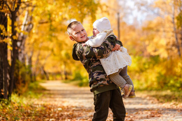 the older brother hugs the little sister. beautiful children in autumn against the background of yellow leaves