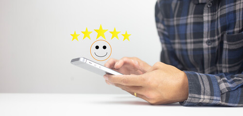Good review feedback satisfaction concept with hand of customer  choosing smiling face and five stars icon on smartphone and copy space background