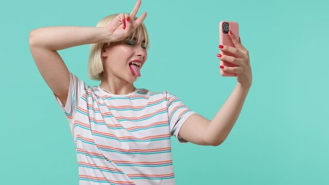 Vivid young blonde short haircut woman 20s years old wears striped t-shirt doing selfie shot on mobile phone post photo on social network isolated on pastel plain light blue background studio portrait