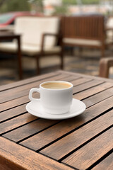 White coffee cup and saucer on wooden table on street cafe terrace.