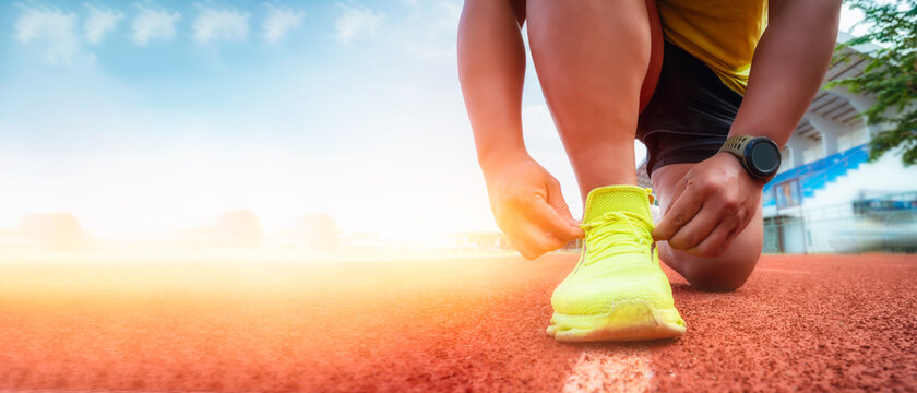 Runner using starting block to start his run on race track. Young man running in the  race track. Young man tying shoelaces preparing to exercise. Active person outdoors at the dusk in summer.