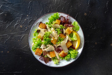 Chicken Caesar salad, overhead shot on a black background. Romaine leaves, crispy croutons and chicken fillet meat