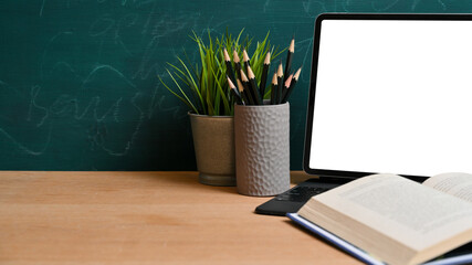 Opened book on tablet blank screen mockup and empty space on wooden table over chalkboard