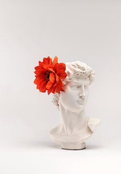 White antique plaster head with a flower on a light background.