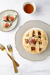 A sweet fig tart pastry on a sophisticated plate, two golden dessert spoons, honey, cut figs on a marble surface, top view