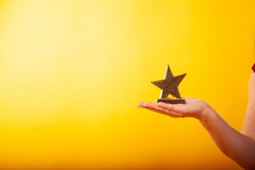 a woman holds a statuette in the form of a star in her hand on a boat in isolation on a yellow background. The concept of a movie star of victory or discounts