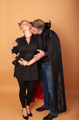 a man and a woman in the form of Count Dracula vampire and vampire witches depict biting in the neck on a beige background on Halloween