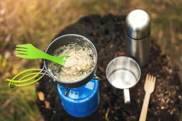 camping meal - preparing oatmeal porridge on portable gas burner outdoors
