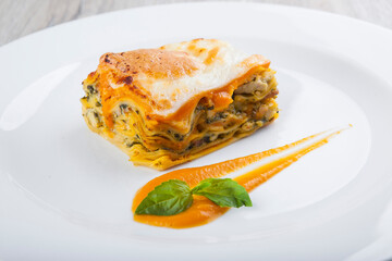 Italian lasagna with meat on a white plate with sauce and basil