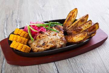 fried pork with fried potatoes and corn in a pan
