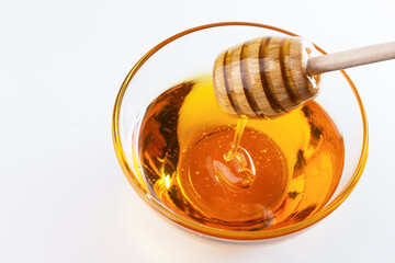 Fototapeta na wymiar Sweet honey. Healthy organic honey dripping from wooden honey dipper in a bowl on white background. Sweet healthy dessert.