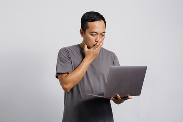 Shocked Asian man looking at laptop with hand covering his mouth