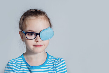 Child girl with an occluder on the eye in a striped jumper on a light background.