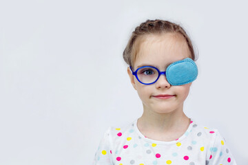 Child girl with an occluder on the eye in a striped jumper on a light background.