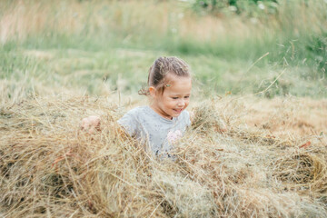Naklejka na ściany i meble Little girl 3-4 years old jumps and plays in hay stack, throwing it up. Motion blur